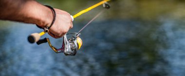 Fisherman on the river bank. Man fisherman catches a fish. Fisherman in his hand holding spinning. Fisherman hand holding fishing rod with reel. Fishing Reel. Fishing rod with aluminum body spool. clipart