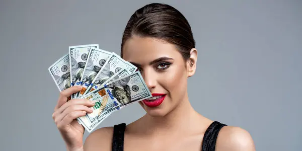 Portrait of a young girl covering her face with money banknotes. Girl holding cash money in dollar banknotes. Woman holding lots of money in dollar currency. Woman with dollars in hand.