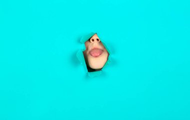 Çocuk dilini duvardaki delikten gösteriyor. Yırtık bir kağıtta dilini gösteren komik çocuk portresi. Dilini gösteren yakın plan erkek yüzü. Çocuk dilini kağıttaki delikten çıkardı..