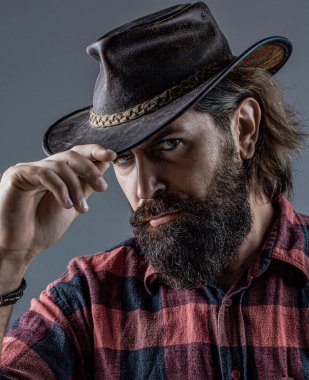 Kovboy şapkasını ayarlayan yakışıklı genç adam. Şapkalı kovboylar. Yakışıklı sakallı maço. Tıraşsız kovboylar. Amerikan kovboyu. Deri kovboy şapkası..
