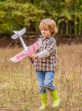 Çocuk anaokulu öğrencisi sokakta oyuncak bir uçak fırlatıyor. Mutlu çocuk oyunu. Mutlu çocuk dışarıda oynuyor. Mutlu çocuk uçakla oynuyor. Uçağı olan küçük çocuk..