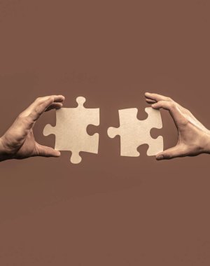 Yapbozu birbirine bağlayan yapbozun yakın eli. Yapbozun parçalarını tutan ve birleştiren adamlar. İki el yapboz parçasını birbirine bağlamaya çalışıyor.