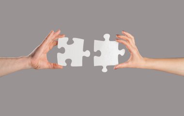Bulmacalar. Erkek ve kadın elinde bir yapboz tutuyor. İş çözümleri, başarı ve strateji kavramı. Eller bulmacayı birbirine bağlıyor. Erkeğin ve kadının eli yapbozu katlıyor, yakın plan..