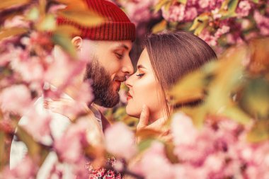 Sevgililer bir sakura 'da sarılıyorlar. Aşk, gençlik, mutluluk konsepti. Açık havada aşık bir çift. Genç şık moda çiftlerinin şehvetli açık hava portresi. Parkta kucaklaşan iki aşık..