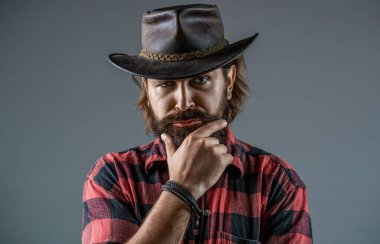 Ekose gömlekli kovboy tarzı. Deri kovboy şapkası. Kovboy şapkasını ayarlayan yakışıklı genç adam. Şapkalı kovboylar. Yakışıklı sakallı maço. Tıraşsız kovboylar. Amerikan kovboyu.
