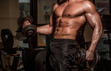 Eğitimdeki güçlü atletik adam halterle kaslarını şişiriyor. Mükemmel bisepsleri, kıvrımları, trisepsleri ve göğsü olan güçlü bir vücut geliştirici. Spor salonunda dambılı kaldıran adam kaslar ve dambıllar için egzersiz yapıyor..