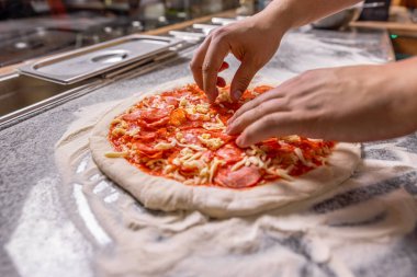 Aşçı mutfakta. Adam pizza hazırlıyor. Pişiren el pizza yapar, sosisi üstüne koyar. Domates soslu pizza hamuruna el peyniri serpiyorum. Şef pizzaya sucuk ve pepperoni dilimleri koyar..