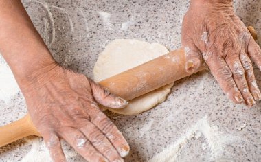 Ev yapımı hamuru kapat. Kadın elleri, masanın üzerinde un, fırın arka planı ve üst görünümü olan oklavaları yuvarlayıp duruyor. Mutfak masasına hamur döken adam, kapat..