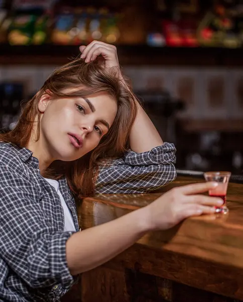 stock image Portrait of drunk woman with glass of alcohol sitting t table at pub. Young woman drinking alcohol in bar. Scotch whiskey glass isolated at bar or pub in alcohol abuse and alcoholic concept.