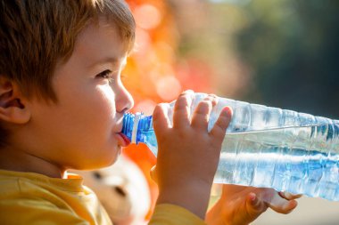 Elinde bir şişe maden suyu olan bir çocuğun portresi. Erkek şişe su. Elinde taze su şişesi tutan genç bir çocuk. Susamış küçük çocuk, bebek su içiyor..