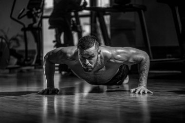 Kaslı bir adam spor salonunun arka planında şınav çekiyor. Spor. Siyah ve beyaz.