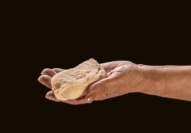 Elinde turta tutan yaşlı bir kadın, siyah arka planda hamur işi. Siyah arka planda hamur tutan kadın elleri. Elleri temiz ve bitmiş bir hamur tutuyor. Eller hamuru pişirmeye hazır, yakın plan..