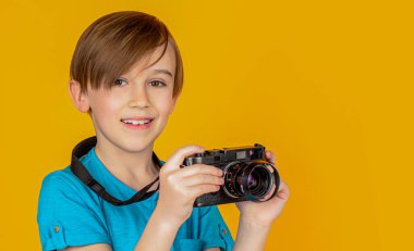 Sarı arka planda fotoğraf çeken küçük bir çocuk. Eski model bir kamera kullanarak fotoğraf çeken küçük bir çocuk. Stüdyodaki çocuk profesyonel kamerayla. Kamera kullanan bir çocuk..