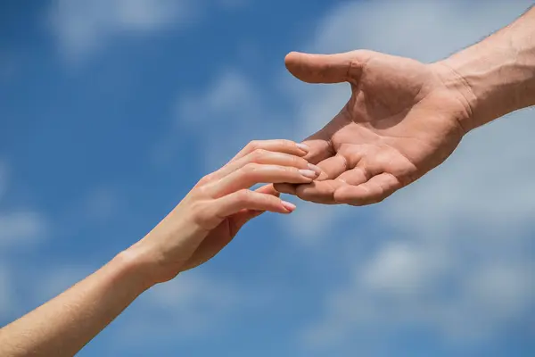 Mavi gökyüzü arka planında kadın ve erkeğin elleri. Yardım eli uzatıyorum. Dayanışma, şefkat ve yardım, kurtarma. Kadın ve erkeğin elleri birbirine uzanıyor, destek oluyor. Yardım eli uzatıyorum..