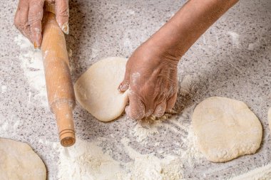 Kadın elleri, masanın üzerinde un, fırın arka planı ve üst görünümü olan oklavaları yuvarlayıp duruyor. Mutfak masasına hamur döken adam, kapat. Ev yapımı hamuru kapat.