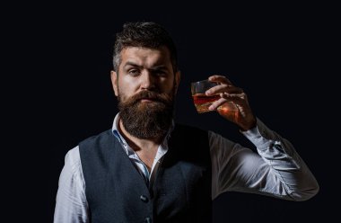 Sakallı adam cam brendi tutuyor. Sakallı konyak. Sommelier içkinin tadını alır. Elinde bir bardak viski tutan bir adam. Viski yudumluyor. Kalın sakallı bir adamın portresi. Maço içki. Degukasyon, tatma.