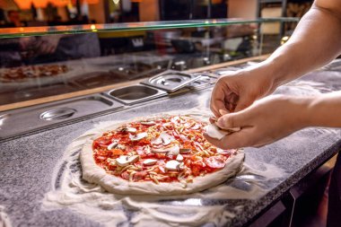 Adam pizza hazırlıyor. Pişiren el pizza yapar, mantarları koyar. Domates soslu pizza üzerine peynir serpmek, pizzaya mantar dilimleri koymak. Şef titizlikle pizzalara malzeme ekler..