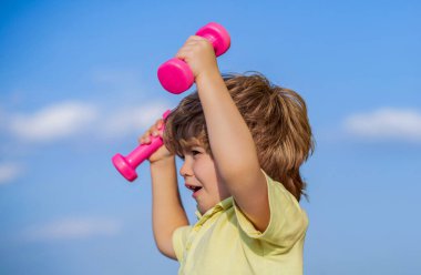 Çocuk dambıllarla egzersiz yapıyor. Küçük çocuklar için spor. Dambılı sportif çocuk. Spor. Fitness, sağlık ve enerji. Sağlıklı bir yaşam tarzı. Arka planda güçlü pazı kasları olan sporcu çocuk..