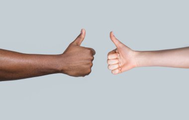 Afrikalı bir adamın eli baş parmağını gösteriyor. Beyaz kadın elleri baş parmağını kaldırıyor. Siyah ve beyaz parmaklar yukarı. Kadın ve erkek ellerinin baş parmaklarını kaldırması. Siyah ve beyaz eller birlikte görünüyor..