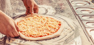 Mutfakta pizza yapan şef fırıncının eli. Masada pizzaya peynir ekleyen adam, yakın plan. Yemek pişirme konsepti, yemek pişirme, pizzacıda rendelenmiş peynir ekleme..