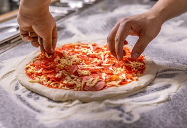 Eller pizza hazırlıyor ya da ev yapımı pepperoni pizza yapıyor. Pişiren el pizza yapar, sosisi üstüne koyar. Domates soslu pizza hamurunun üzerine peynir serpiyorum..