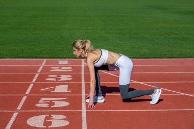 Girl at the start is ready to run and win. Female athlete alone on the athletic track, sprint running. Athlete on the starting. Young sportswoman sprint on a running track outdoors on stadium. clipart