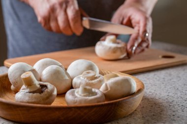 Bir kadın elleri ahşap masada mantar kesiyor. Şef kesme, mantar doğrama şampiyonu yakın plan. Sağlıklı sebze pişiren eller. Mutfakta bıçakla mantar kesen adamın elleri..