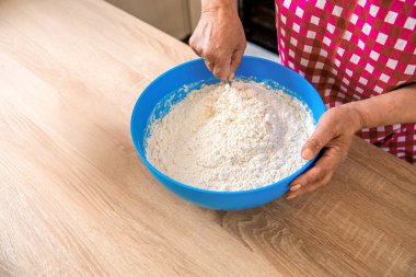 Kadın kaşıkla un karıştırıyor. Elle hamur yoğuran bir kadın. Mavi metal bir kasede kadın eli ve hamuru. Kadın aşçı mutfak masasında hamur hazırlıyor..