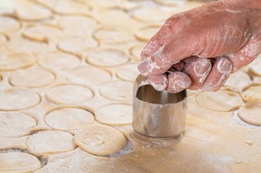 Hamurun büyük bir kısmını pişirmek için hazırlıyorlar, masanın üstünde ve şef demir bir şekille küçük daireler çiziyor. Hamur çemberleri kesiyor metal, yuvarlak bir bıçak..