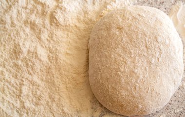 Un ile pizza hamuru yapıyorum. Masada çiğ hamur ve un var. Ekşi hamuru yakın plan. Un kaplı bir yüzeyde ekmek ya da pizza için maya hamuru. Ekmek pişiriyorum. Hamuru yoğuruyorum..