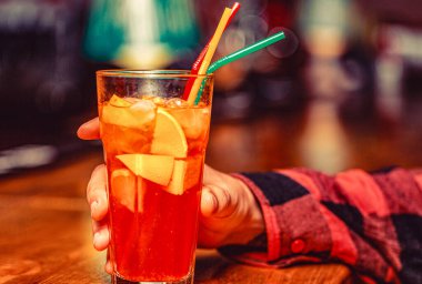 Bir bardak negroni kokteyli tutan adam. Bir bardak Aperol sprey kokteyli ile erkek eli. Parlak çubuk arkaplanı üzerinde tüp olan kokteyl.