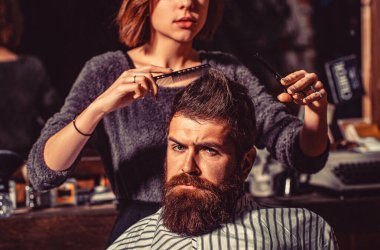 Kadın berber, makas kullanarak saç stilini zayıflatıyor. Berber dükkanında sakallı adamın saçını kesen kız. Bakım, erkeksi güzellik..