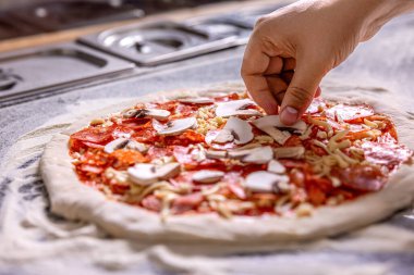 Masada çiğ pizza malzemeleri var. Şef pizza yapıyor. Eller pizza hazırlıyor ya da ev yapımı pepperoni pizza yapıyor. Pişiren el pizza yapar, sosisi üstüne koyar..