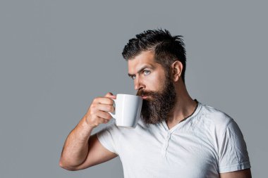 Günaydın, elinde çay tutan adam. Yakışıklı sakallı erkek elinde kahve ve çay tutuyor. Bir fincan taze kahveyle hippi adam. Elinde kupa tutan sakallı bir adamın yakın portresi..