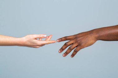 Beyaz kadın ve Afrikalı adam gri arka planda parmaklarını birbirine değdiriyorlar. Irkçılık konsepti. Nazikçe uzanmış iki el dokunmak istiyor. Bir an için gel..