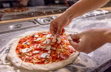 Aşçı mutfakta, pizzanın malzemelerini koyuyor. Adam pizza hazırlıyor. Pişiren el pizza yapar, mantarları koyar. Şef titizlikle pizzalara malzeme ekler..