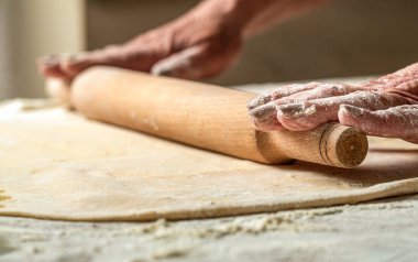 Merdaneyle hamuru hazırlayan kişi. Kadın eli merdaneyle hamuru yuvarlıyor. Masadaki ev yapımı fırın için merdaneli hamuru yuvarlayan adama yakın çekim..