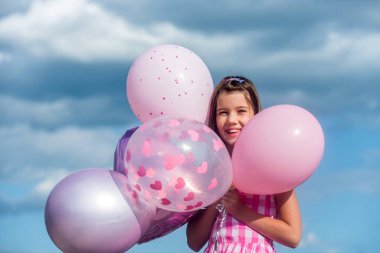 Mutlu çocuk balonları dışarıda. Balon tutan neşeli şirin kız, mutlulukla mavi gökyüzü. Eller hava balonlarını tutuyor. Gökyüzü arka planında balon tutan gözlüklü güzel küçük kız.