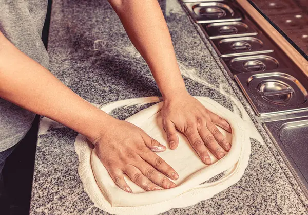 Masada nefis bir pizza üretimi. Şef pizza hamuru elleri hazırlıyor. Pizza hamuru yuvarlanıp yoğuruluyor. Hamur yoğuran elleri pişir.