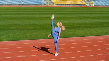 Stadyumda esneme hareketleri yapan bir kız. Stadyumda bacak ayrımı, esneme hareketleri. Atletik fitness kadın bacağı dışarıda egzersiz yapıyor. Genç, sıska kadın bacaklarını esnetiyor..