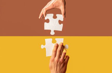 İnsan eli, yapboz parçalarını bir araya getiriyor. İki el yapboz parçasını birbirine bağlamaya çalışıyor.