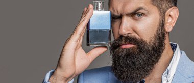 Parfüm kullanan yakışıklı genç adam. Sakallı adam lüks parfüm sıkıyor, yakın plan. Resmi takım elbiseli bir adam, bir şişe parfüm, yakın plan..