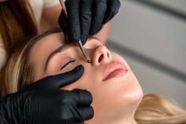 Kozmetik uzmanı yüzünü temizliyor. Siyah başlık çıkarıcı kullanan eller. Yüz derisinin kaşık uno ile mekanik temizlenmesi, yağ çıkarılması, siyah noktalar. Cilt soyma, güzellik uzmanı, estetikçi tarafından temizleme..