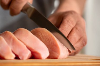 Kadın mutfakta tavuk kesiyor. Şef eller tavuk filetosunu bıçakla kesti. Tavuk kesme teknolojisi. Erkek elleri ahşap tahtada tavuk filetosu kesiyor, masa, yakın plan.