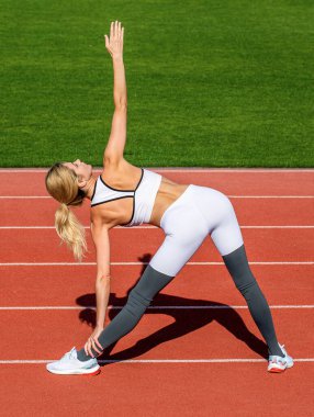 Koşmadan önce esneme hareketleri yapan genç bir kadın. Stadyumda koşmadan önce esneme hareketleri yapan sporcu kadın. Spor kıyafetli bir kadın şehir stadyumunda spor yapmadan önce esneme hareketleri yapıyor..