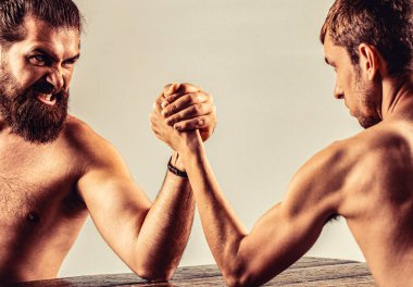 Bilek güreşi. Güçlü kaslı bir adam zayıf bir adamla bilek güreşi yapıyor. Bilekleri zayıf, kolları güçlü. Erkek eli kenetlenmiş bilek güreşi, güçlü ve zayıf, eşit olmayan maç.