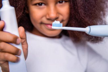 Sağlıklı dişler, diş macunu. Küçük kız, diş fırçası. Çok ırklı bir kız dişlerini elektrikli bir diş fırçası ile fırçalar. Küçük kız diş fırçası yakın plan. Küçük tatlı Afrikalı Amerikalı kız dişlerini fırçalıyor..