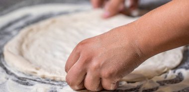Eller pizza yapmak için hamur yoğurur. Masada pizza hamuru yoğuran bir kadın, yakın plan. Pizza hamuru yuvarlanıp yoğuruluyor. Hamur yoğuran elleri pişir, beyaz buğday unu serpiştir.