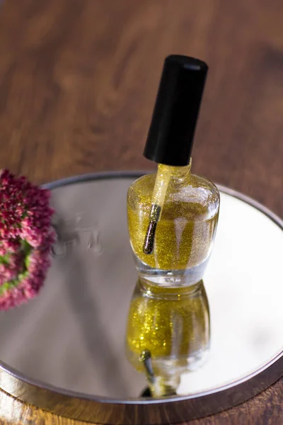 A translucent gold glitter nail polish with a rose red flower that reflects in the mirror