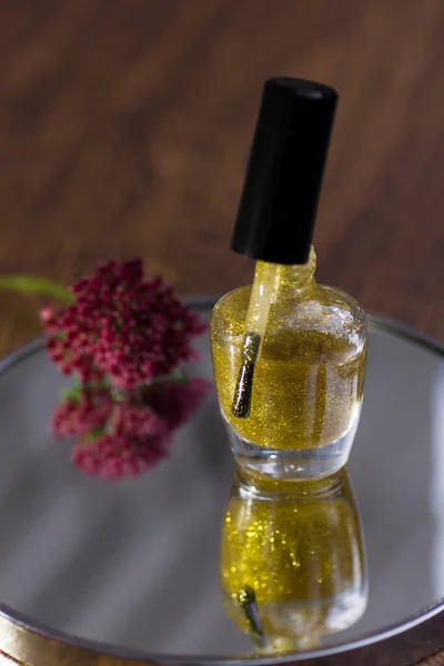 A translucent gold glitter nail polish with a rose red flower that reflects in the mirror